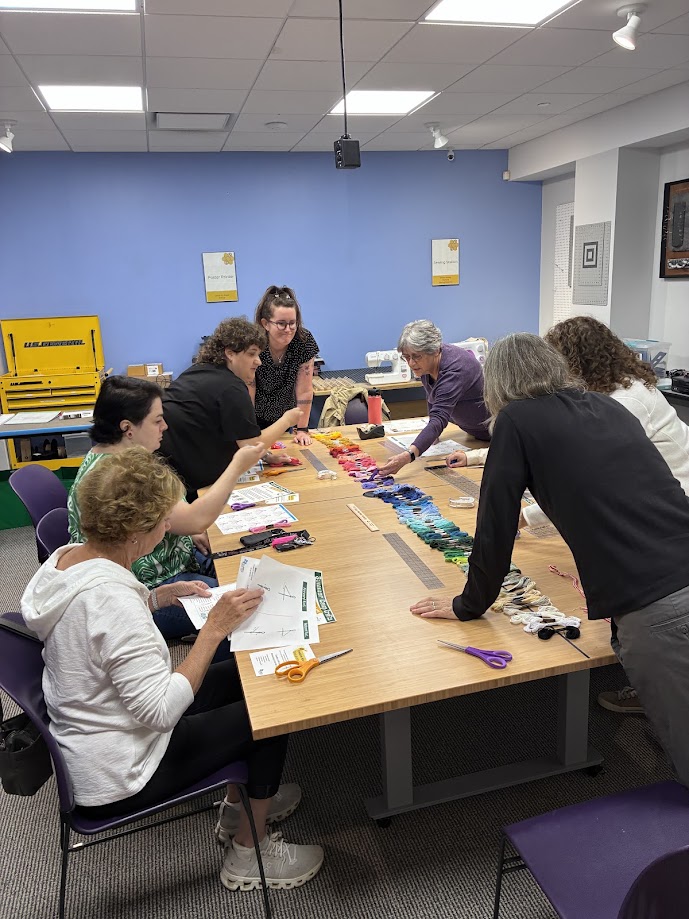 Photograph of program participants leaning across a table to choose colors for friendship bracelets.
