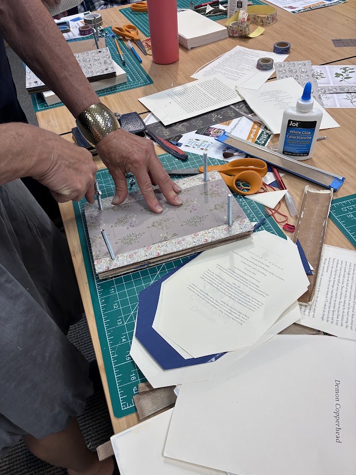 A crafter assembles layers of a flower press made out of a recycled hardcover book.